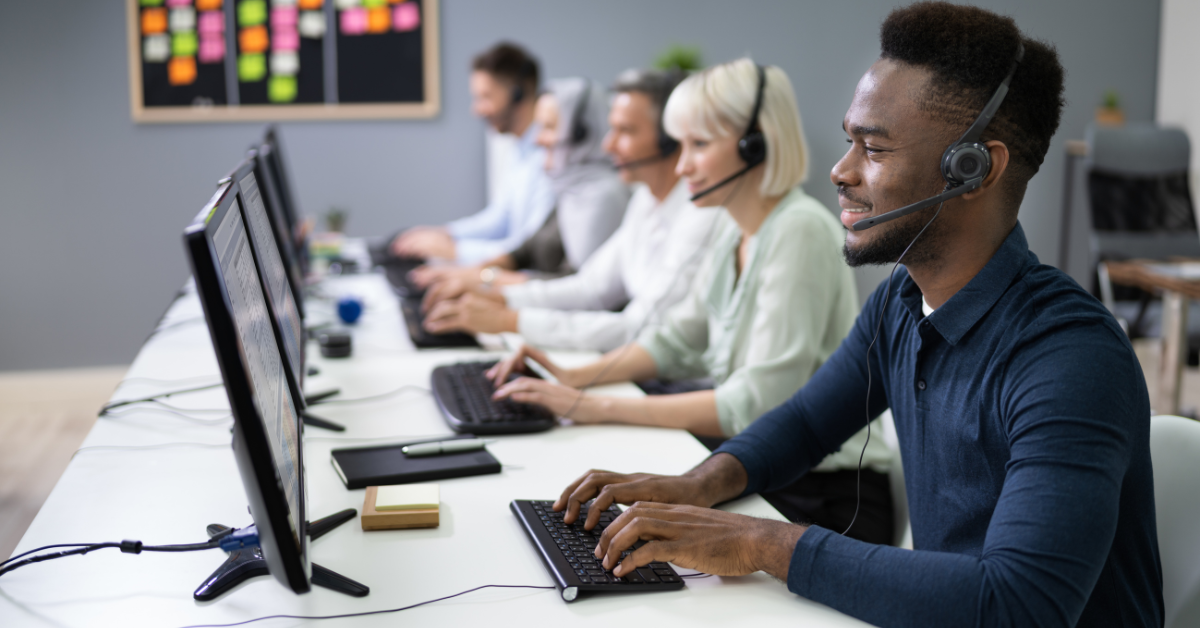 A row of smiling call center workers wearing headsets in front of computers