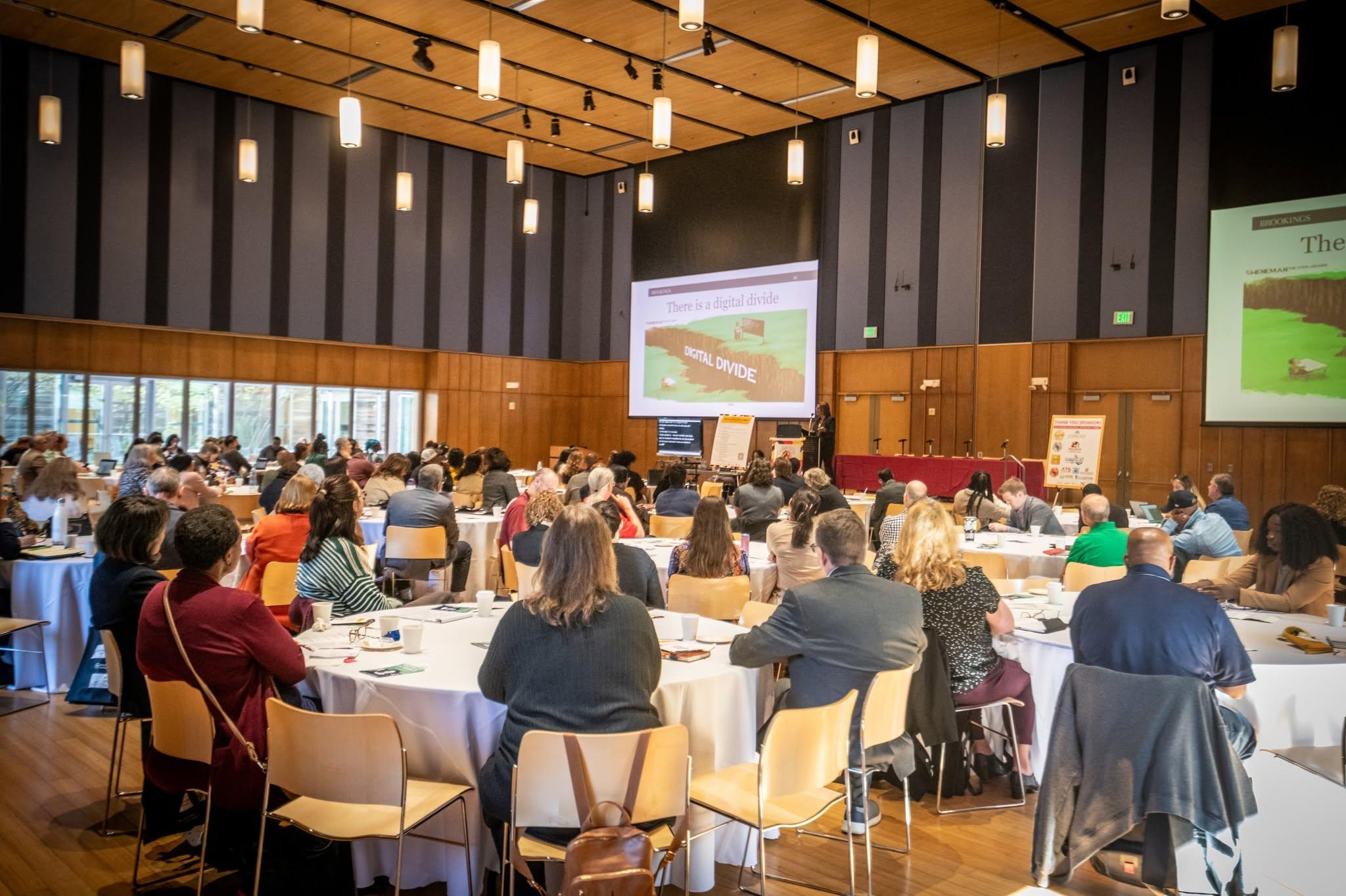 Widescreen picture of attendees facing towards a large projector at the 2025 Digital Opportunity Summit.