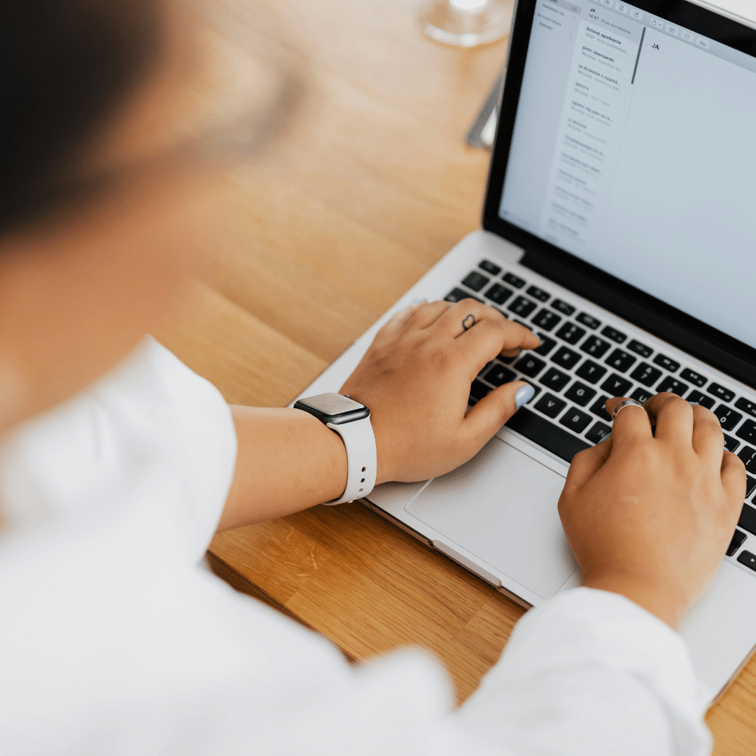 A person typing on a laptop, wearing a white shirt and watch.